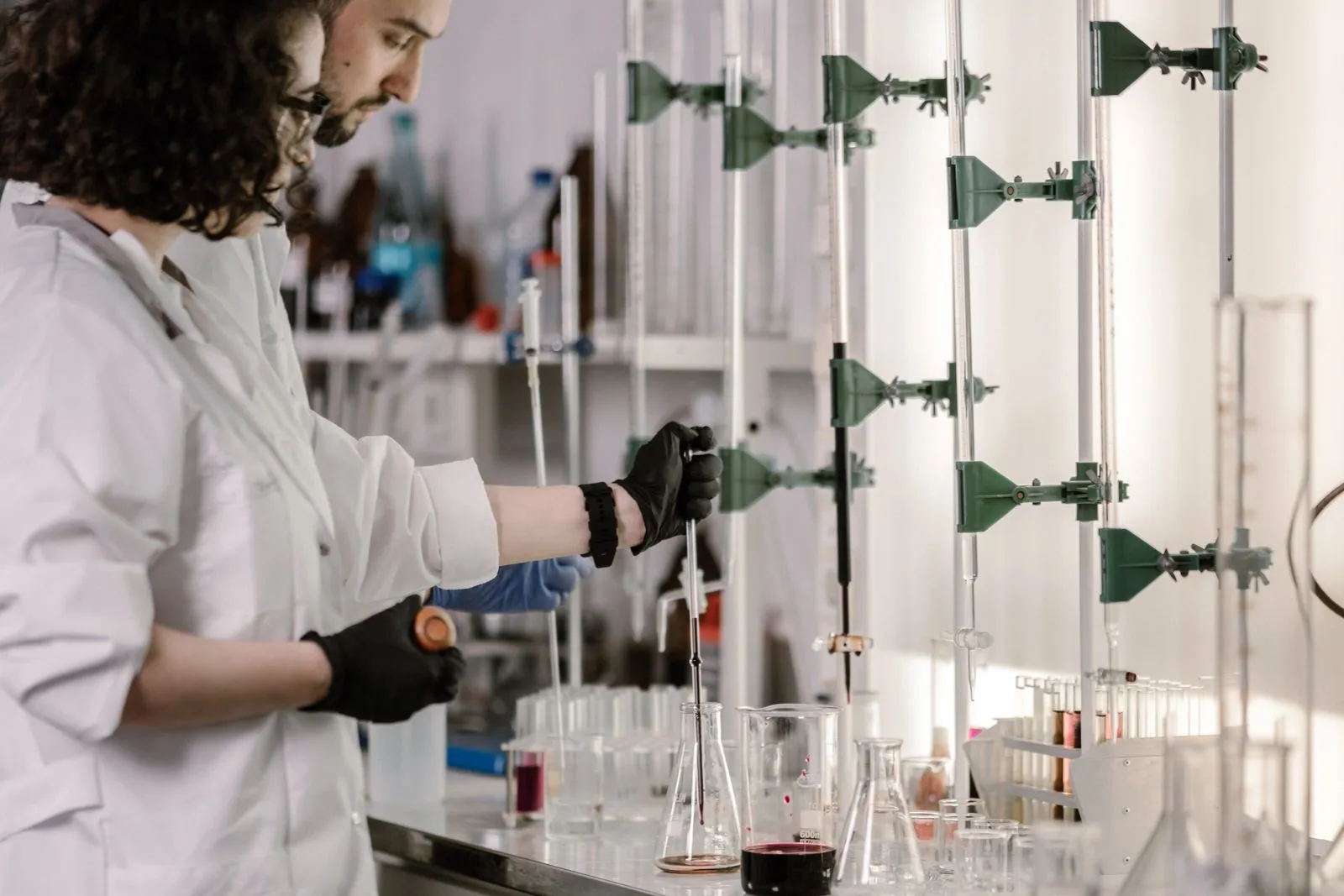 Deux personnes en blouse et gants manipulent de la verrerie dans un laboratoire