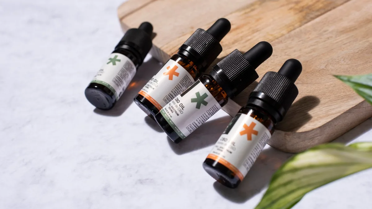 Quatre flacons d’huile CBD avec pipettes, disposés à côté d’une planche en bois