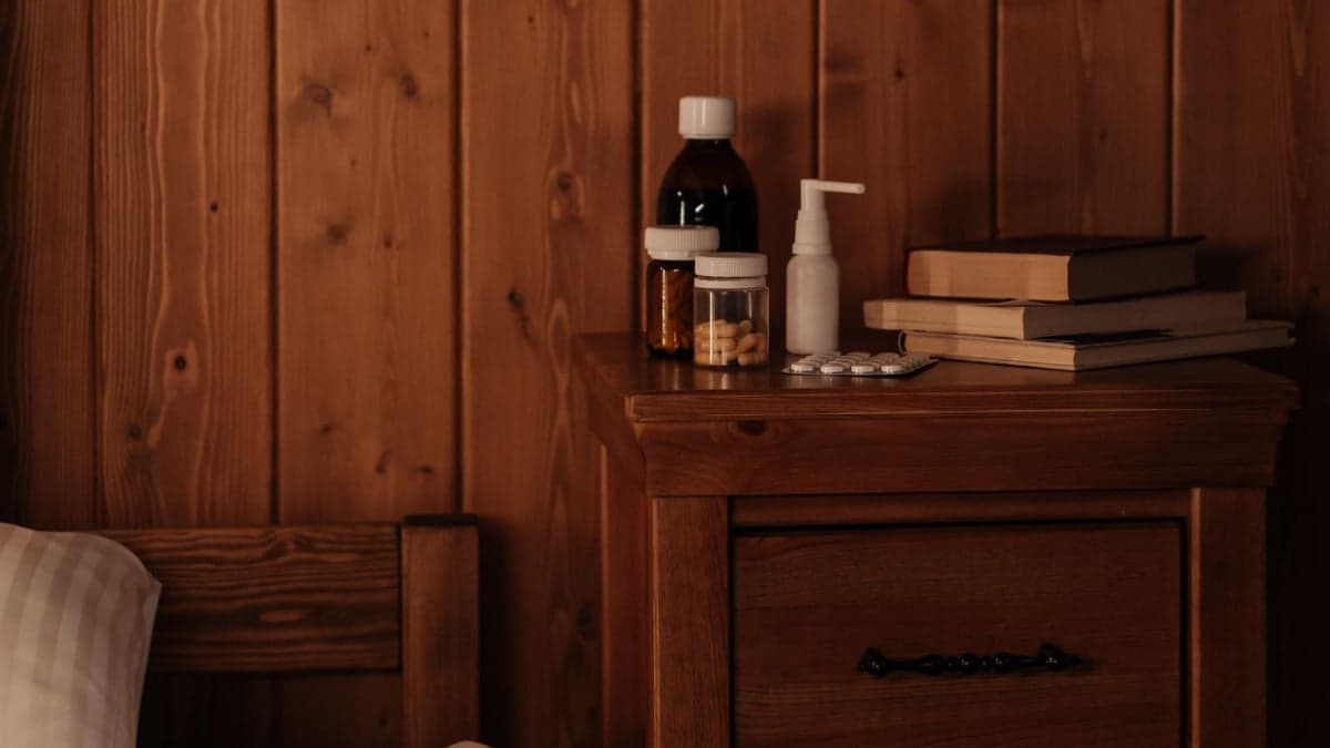 Flacons, plaquette de comprimés et livres posés sur un chevet en bois à côté du lit