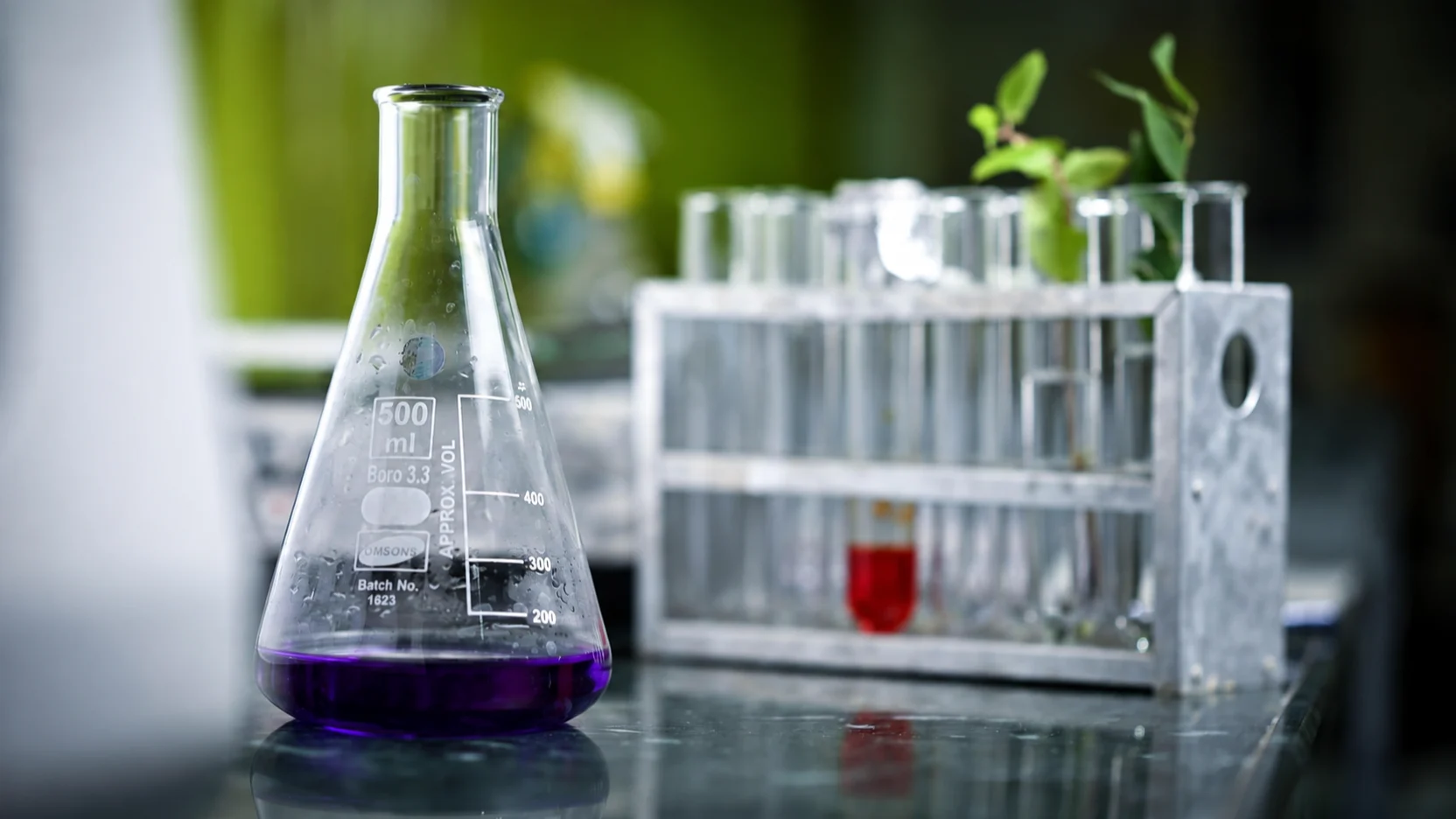 Fiole de laboratoire contenant un liquide violet, avec éprouvettes à l’arrière-plan